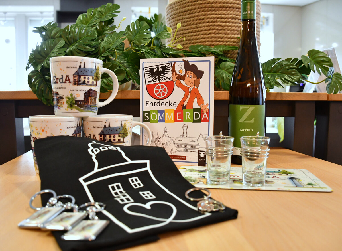 Souvenirs von Sömmerda in der Tourist-Information Sömmerda Zu sehen sind Souvenirs von der Sömmerdaer Tourist Information. 3 Tassen mit Sömmerdaer Sehenswürdigkeiten (FineArt), ein "Entdecke Sömmerda" Heft, Wein vom Weingut Zahn, Schnapsgläser mit Logo Sömmerda, Frühstücksbrettchen (FineArt), Jutebeutel in schwarz mit dem Erfurter Tor in weiß, Schlüsselanhänger mit FineArt