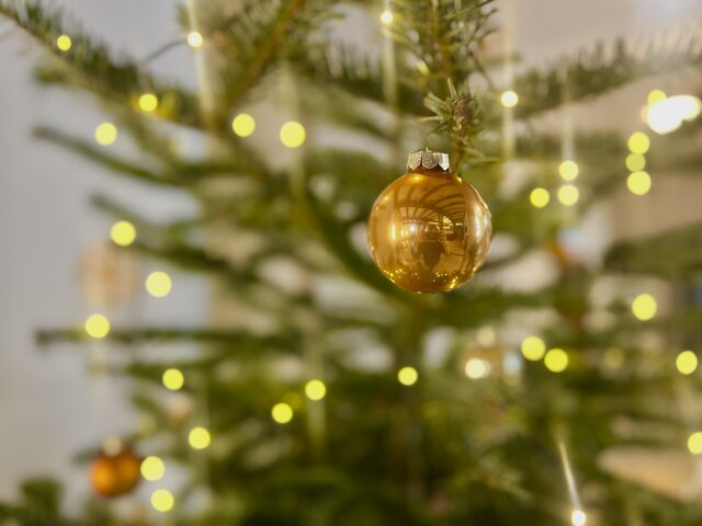 Goldene Kugel am Weihnachtsbaum mit Lichterketten Goldene Christbaumkugel an einem geschmückten Weihnachtsbaum mit warmweißen Lichterketten im Hintergrund, unscharfer Hintergrund sorgt für stimmungsvolle Atmosphäre.