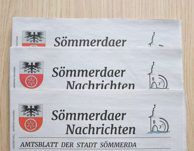 Drei Exemplare des Amtsblattes liegen mit der Titelseite aufgefächert auf einen Tisch. Zu sehen ist der Kop der Amtsblätter mit dem Wappen der Stadt Sömmerda (ein schwarzer Adler im oberen weißen Teil und ein altes Rad im unteren roten Teil), dem Logo der Stadt mit stilisiertem Erfurter Tor und Mühlrad in Form einer CD sowie der Aufschrift Sömmerdaer Nachrichten - Amtsblatt der Stadt Sömmerda.