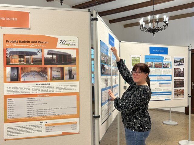 Julia Ansorg, Projektmanagerin des Zweckverbandes, hat die Ausstellung erarbeitet und gestaltet. Ausstellungswände mit Plakaten und Fotos sind im Vorraum des Sitzungssaals im Rathaus im Zickzack aufgestellt. Die Projektmanagerin des Zweckverbandes bestückt eine der Wände noch mit Fotos.
