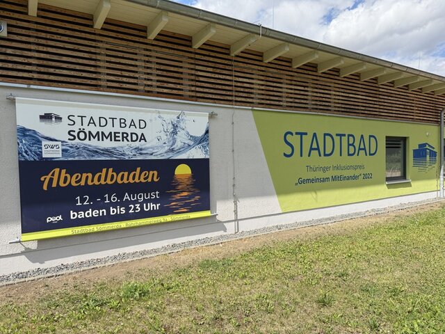Werbung am Stadtbad-Gelände für das Abendschwimmen 2026. An der Frontseite des Empfangsgebäudes im Stadtbad hängt ein großes Plakat. Auf diesem steht unter anderem das Datum, an dem das Abendbaden angeboten wird. Zudem wird auf die verlängerte Öffnungszeit bis 23:00 Uhr an den Tagen des Abendbadens hingewiesen.