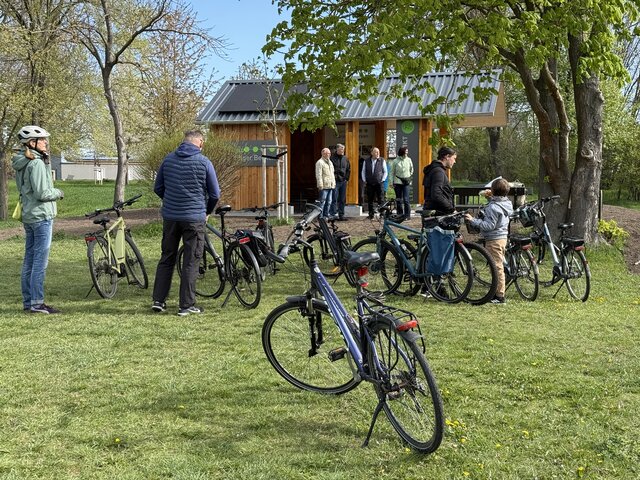 Eröffnung des neuen Radler-Rastplatzes in Leubingen Mehrere Radfahrerinnen und Radfahrer stehen mit ihren Fahrrädern am neu eröffneten Radler-Rastplatz in Leubingen. Im Hintergrund ist die überdachte Holzstation mit Solarmodulen zu sehen.