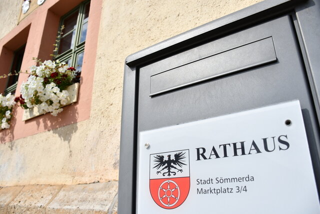 Ausschnitt der Rathausfassade. Ein Ausschnitt der Fassade des Rathauses mit Blumenkästen n Fenstern und dem Briefkasten in Edelstahl-Ausführung. Daran ist ein Schild mit dem Stadtwappen von Sömmerda und den Wörtern Rathaus Stadt Sömmerda, Marktplatz 3/4 angebracht.