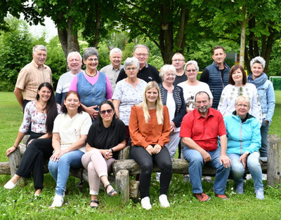Mitglieder des Seniorenbeirates und die Ansprechpartnerin für das ehrenamtliche Gremium bei der Stadt (1. v. l.) im Garten des Bürgerzentrums "Bertha von Suttner". Mitglieder des Seniorenbeirates und die Ansprechpartnerin der Stadtverwaltung für den Seniorenbeirat stehen (hintere Reihe) bzw. sitzen (vordere Reihe) im Grünen auf dem Gelände des Bürgerzentrums im Stadtteil Neue Zeit/Offenhain. Im Hintergrund stehen etliche große Bäume.