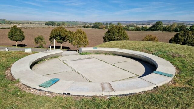 Die Plattform des Fürstenhügels Leubingen. Auf dem Betonring fehlen drei der insgesamt sechs Kupferplatten. Die mit einem Betonring eingefasste große Plattform auf dem Fürstenhügel Leubingen mit Blick in die Landschaft - in dem Fall auf eine Baumreihe, dahinter ein umgeackertes Feld sowie weiter hinten die Autobahn A 71. Auf dem Betonring fehlen drei der insgesamt sechs rechteckigen Kupferplatten.