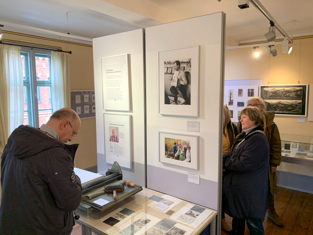 Der Ausstellungsraum um Museum zur Sonderschau. Drei fraue und ein Mann schauen sich an verschiedenen Stellen im Raum Ausstellungsgegenstände wie Fotos, Druckgrafiken und Druckplatten von Rolf Fleischmann an.uckplatten 