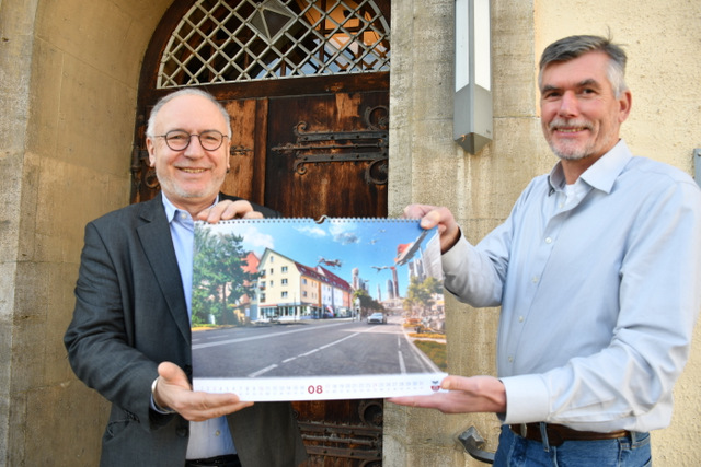 Der Bürgermeister und der Bauamtsleiter zeigen vor dem Rathaus stehend ein Kalenderblatt. Es ist das Kalenderblatt für den Monat August. Mithilfe der KI wurden in das Originalfoto (Blick in die Marktstraße aufs Rathaus) anstelle von Rathaus und der rechten Häuserzeile eine hypermoderne Skyline aus Hochhäusern und Hochhaustürmen ins Bild gebracht. Am Himmel fliegen Drohnen und moderne Luftfahrzeuge. Auf der Marktstraße fahren superschnelle Autos.