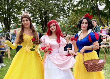 Sogenannte Walking-Acts beim Märchengarten: Drei junge Frauen - zwei verkleidet als Prinzessinnen, eine als Schneewittchen stehen vor der Besucherkulisse mit Blick zum Fotografen.