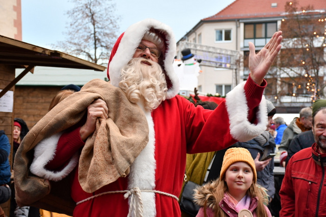 Der Weihnachtsmann steht im roten Mantel, dem Geschenke-Sack über der Schulter und mit ausgestreckter Hand steht umringt von Kindern und Erwachsenen mitten auf dem Weihnachtsmarkt in Sömmerda.