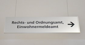 Silbernes Wegweiserschild hängt von der Decke mit dem Aufdruck Rechts- und Ordnungsat, Einwohnermeldeamt